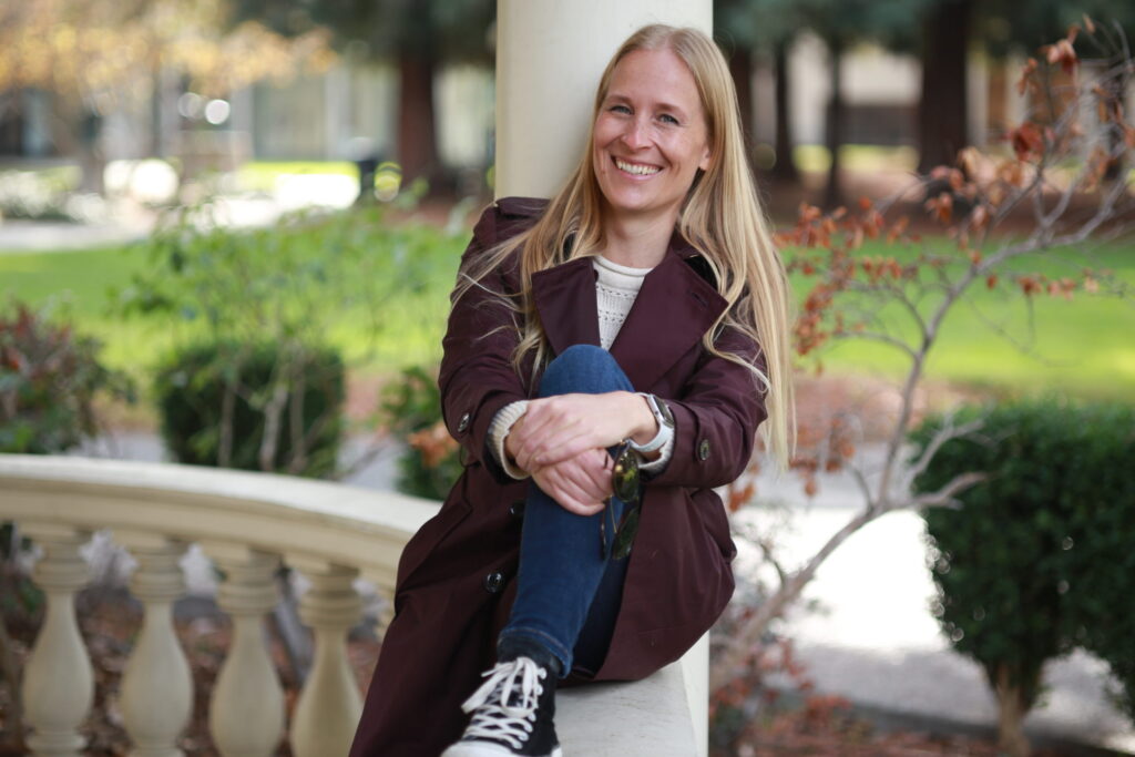 Anna-Kaisa Manolova sitting on a fence, smiling