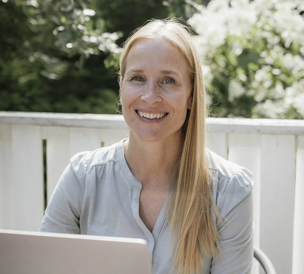 Anna-Kaisa Manolova working outdoors with her laptop and smiling